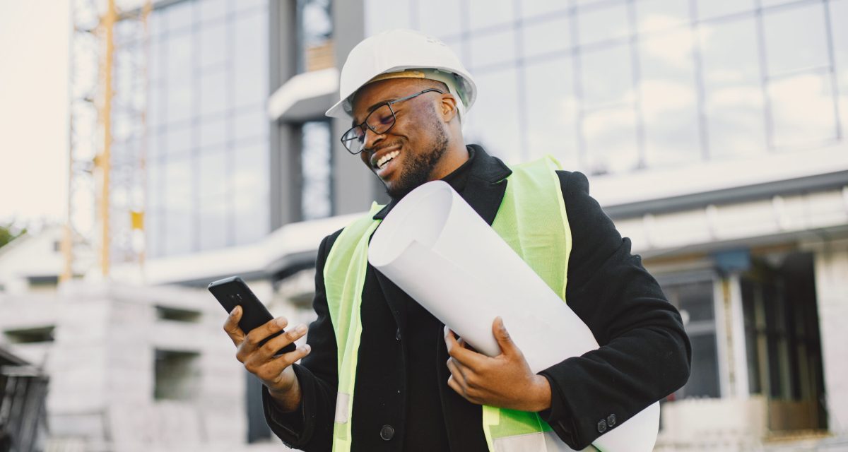 Black architect with project talk by phone Young black race man with blueprint stading near glass building. Talking by phone.